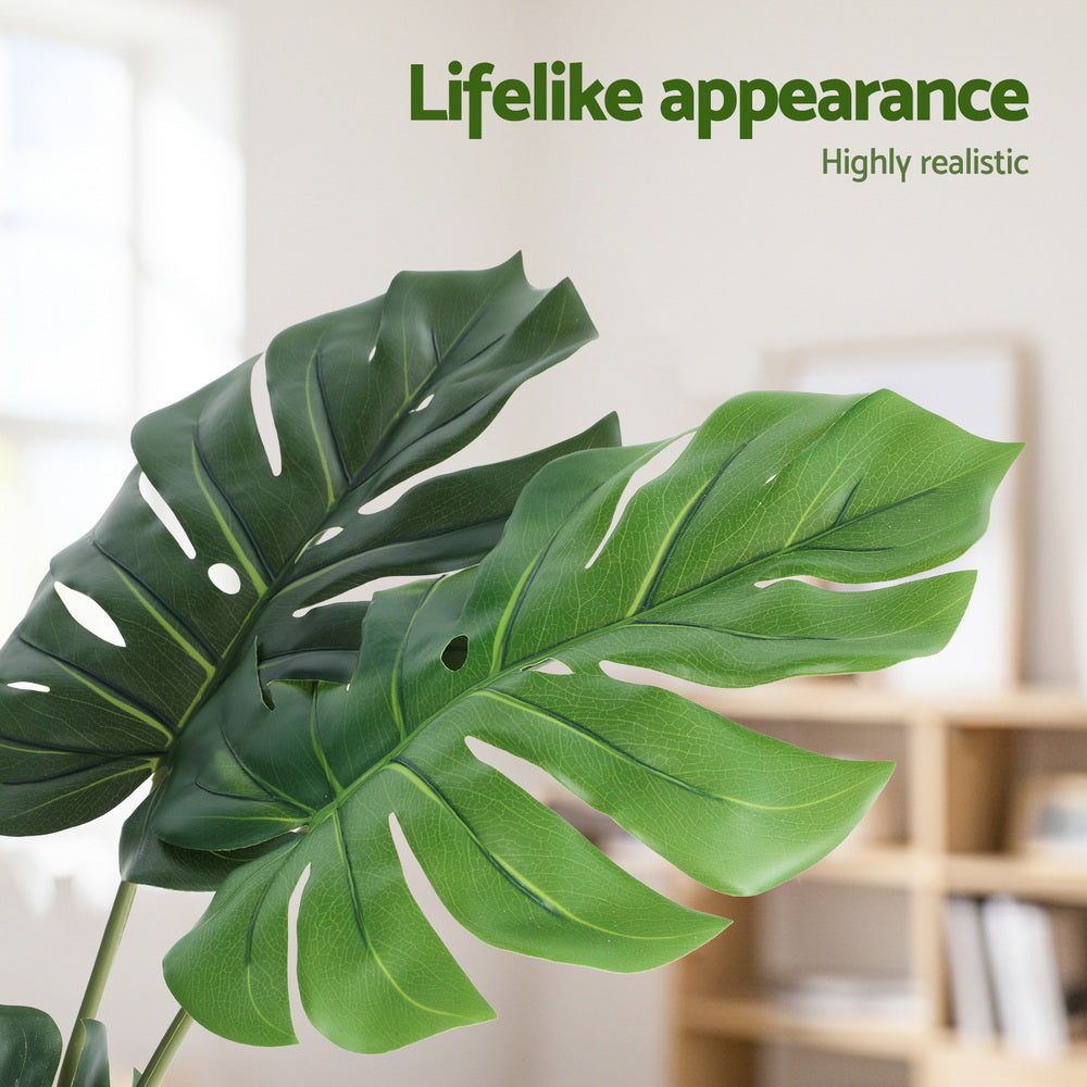 Artificial monstera leaf with a blurred indoor background and text 'Lifelike appearance' and 'Highly realistic'.